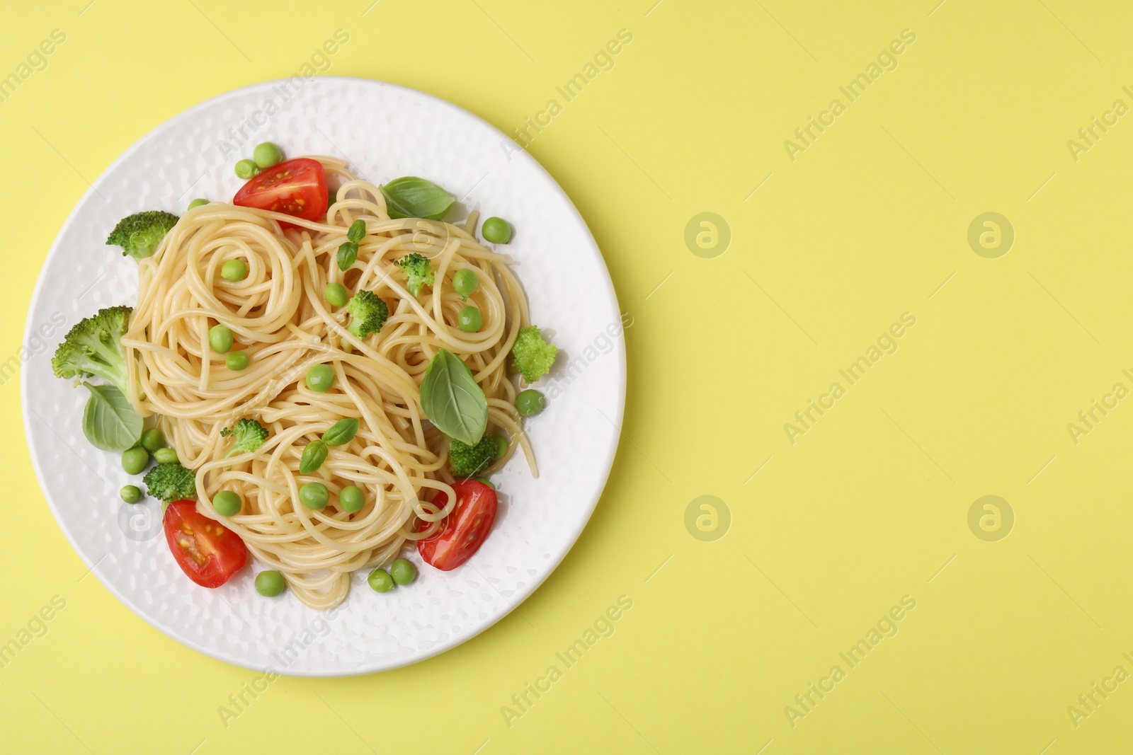 Photo of Plate of delicious pasta primavera on yellow background, top view. Space for text