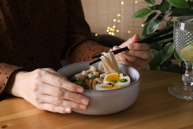 Photo of Woman eating delicious ramen with chopsticks at wooden table indoors, closeup. Noodle soup