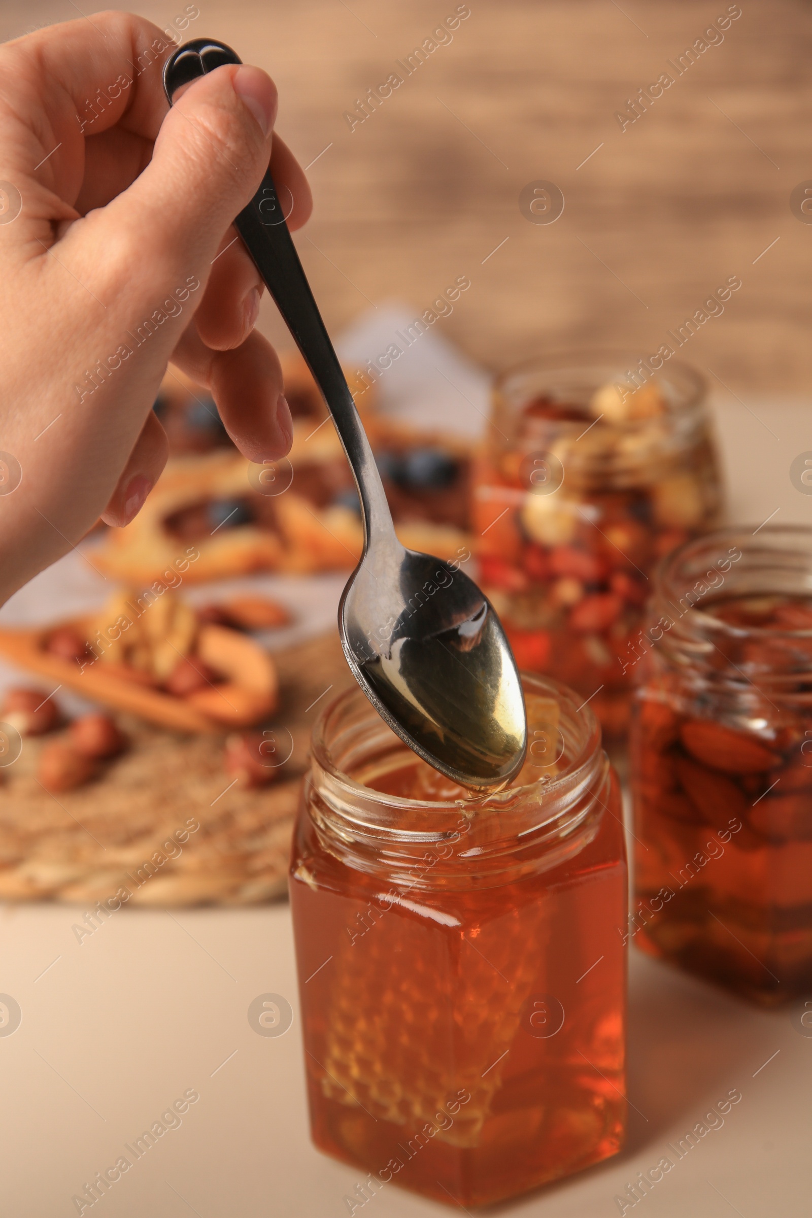 Photo of Woman taking spoon of honey from glass jar at beige table, closeup