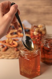 Photo of Woman taking spoon of honey from glass jar at beige table, closeup