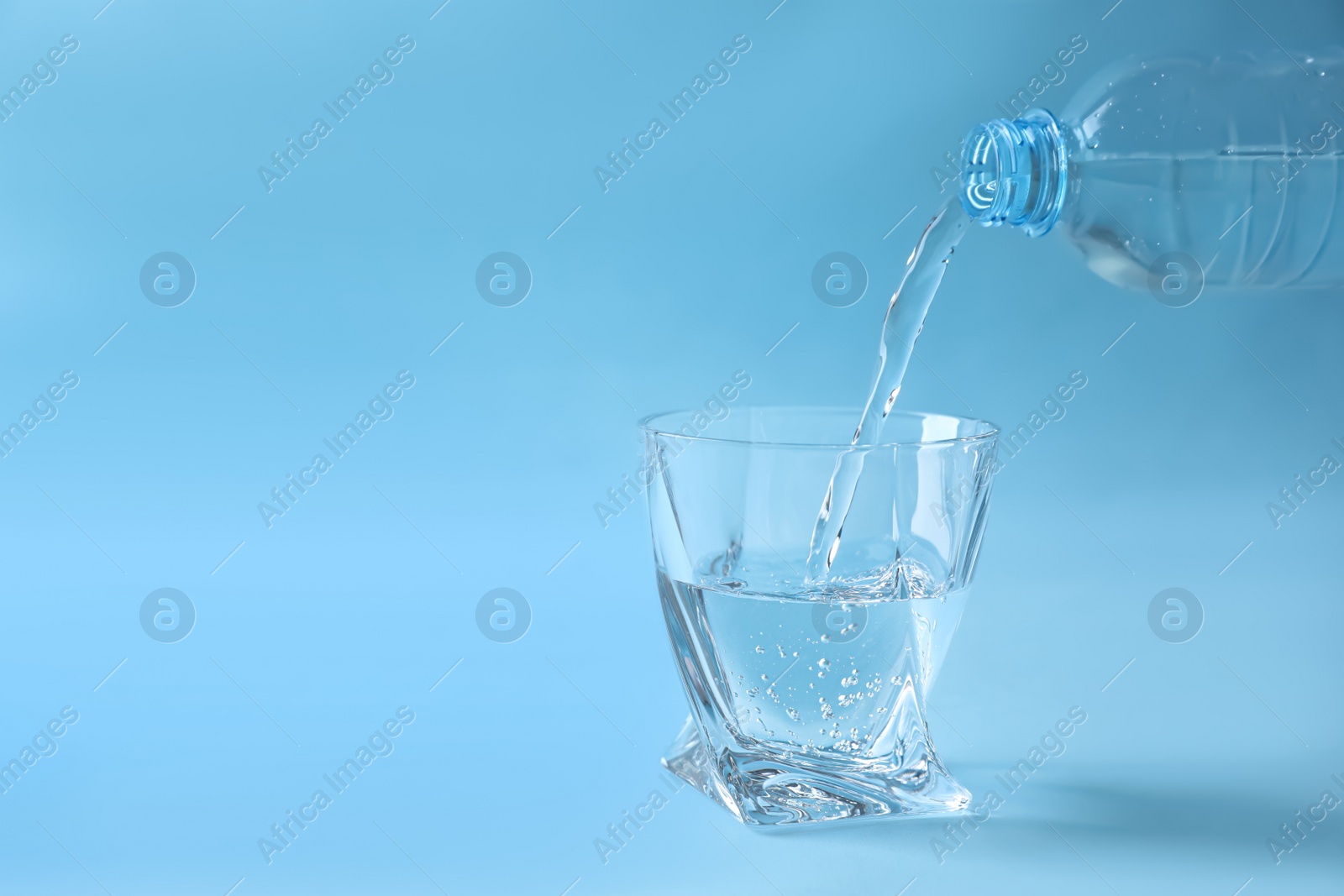 Photo of Pouring water from bottle into glass on light blue background. Space for text