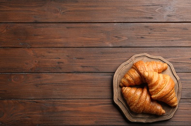 Photo of Board with tasty croissants and space for text on wooden background, top view. French pastry