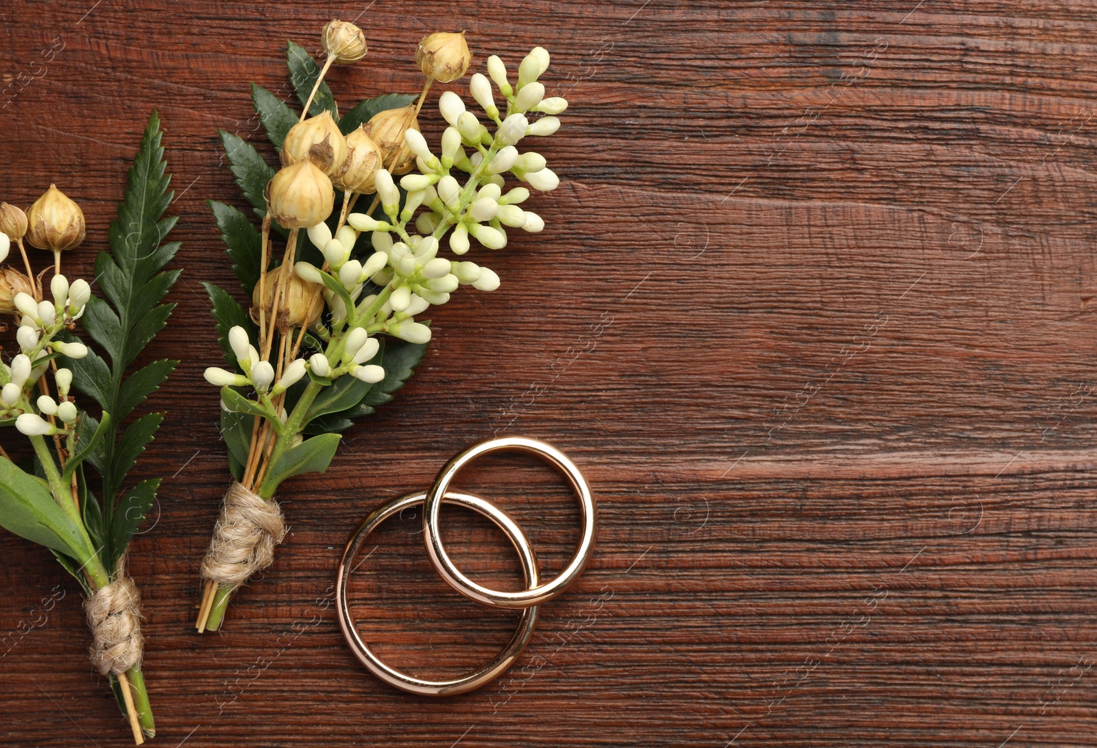 Photo of Small stylish boutonnieres and rings on wooden table, flat lay. Space for text