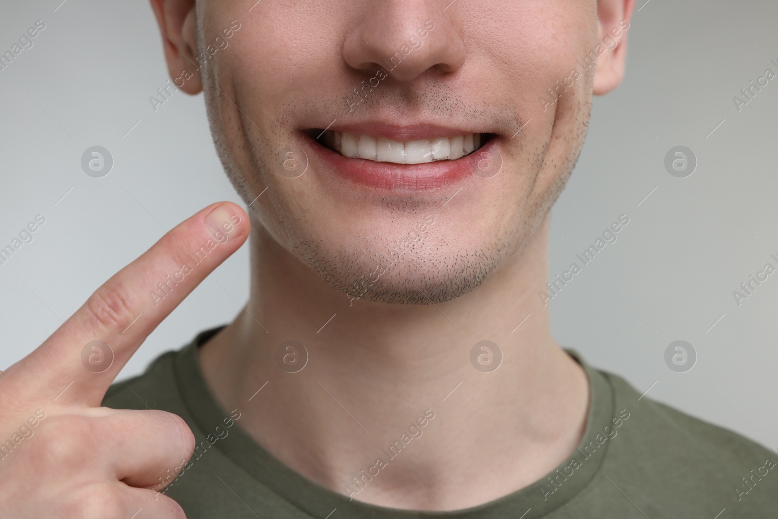 Photo of Young man showing his teeth with whitening strip on light grey background, closeup