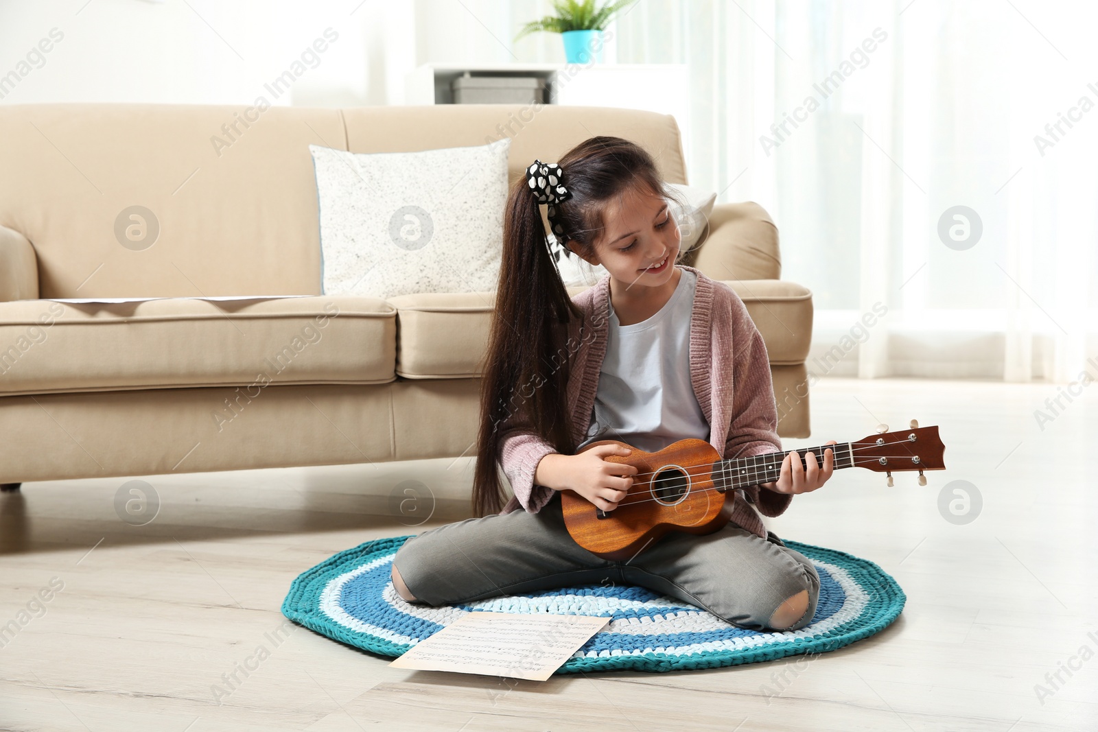 Photo of Cute little girl playing guitar on floor in room