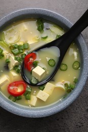 Photo of Bowl of delicious miso soup with tofu and spoon served on grey table, top view