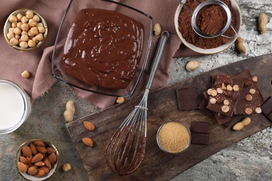Bowl of chocolate cream, whisk and ingredients on grey textured table, flat lay