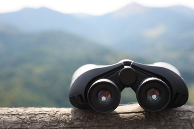 Photo of Modern binoculars on wooden log in mountains, space for text