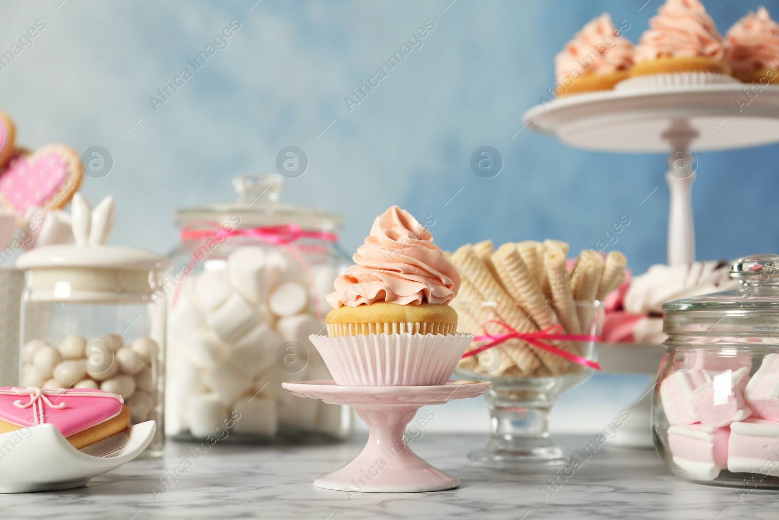 Photo of Stand with cupcake and other sweets on white marble table. Candy bar