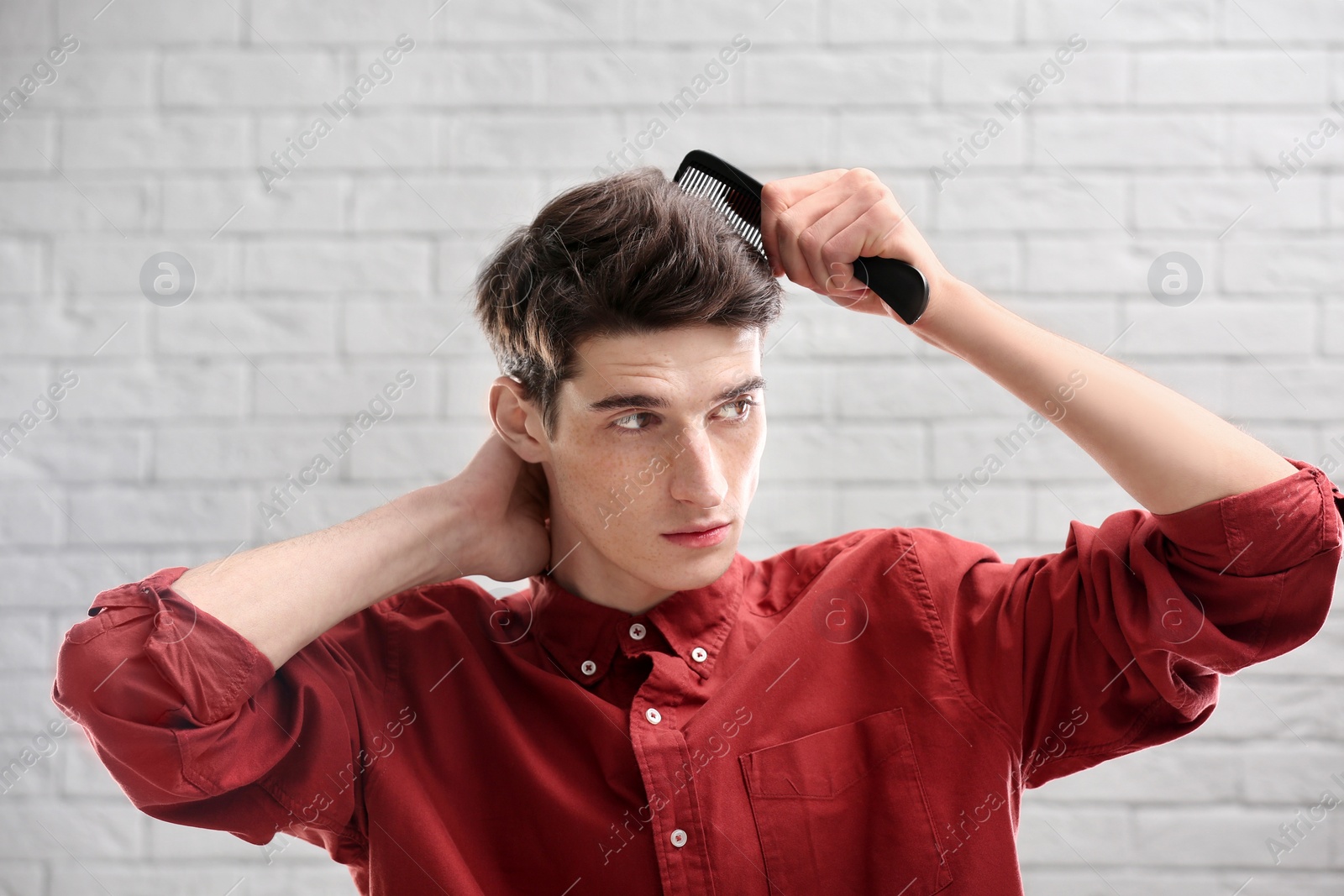 Photo of Portrait of young man combing his hair on brick wall background