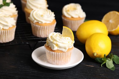 Delicious cupcakes with white cream, lemon zest and lemons on black wooden table, closeup