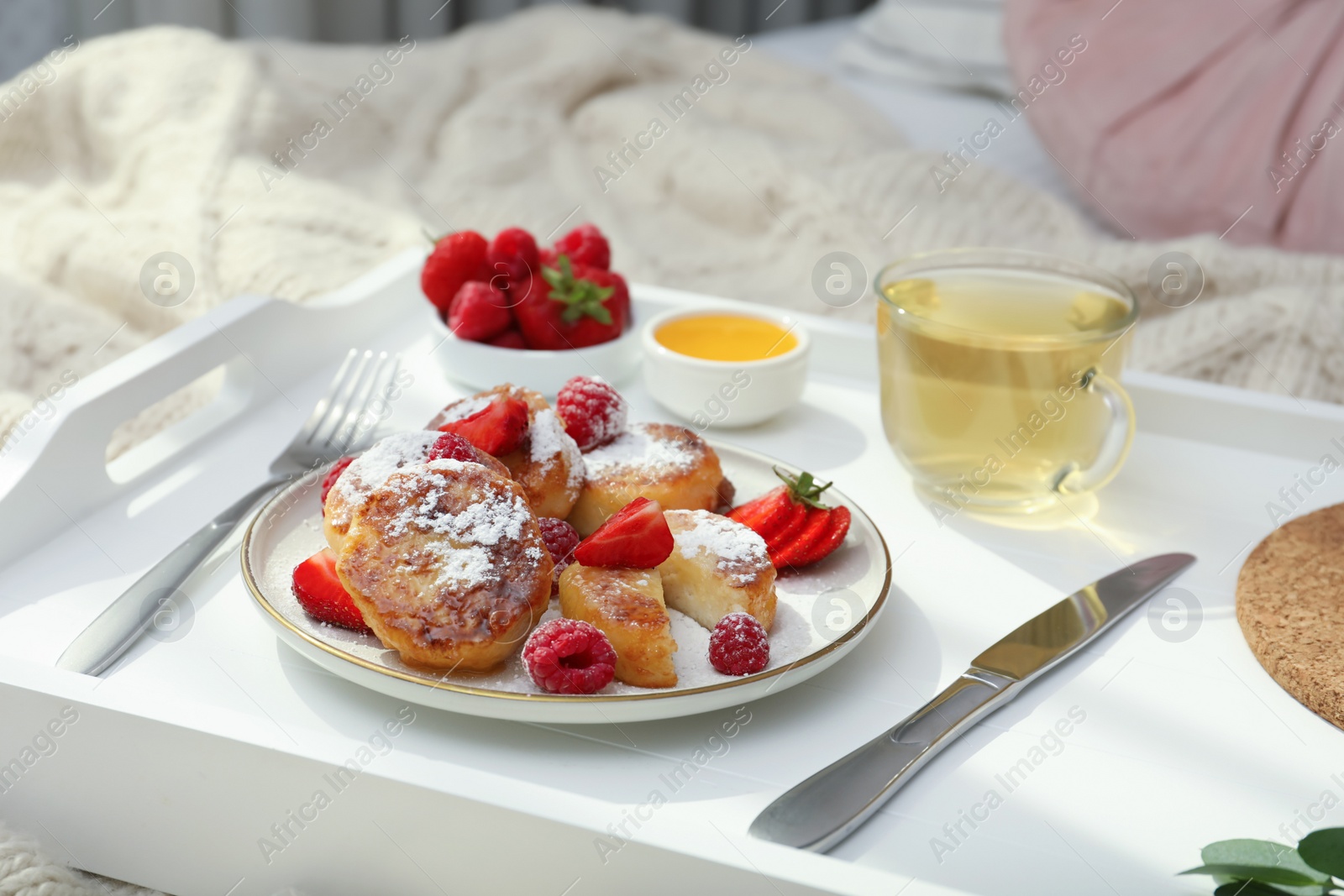 Photo of Tasty breakfast served in bedroom. Cottage cheese pancakes with fresh berries and icing sugar on wooden tray