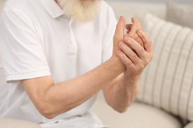 Senior man suffering from pain in hand on sofa, closeup. Rheumatism symptom