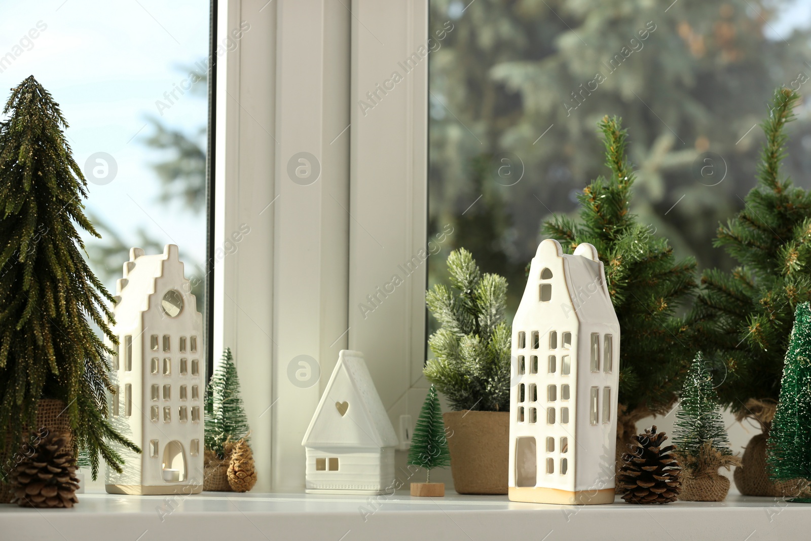 Photo of Beautiful house shaped candle holders and small fir trees on windowsill indoors