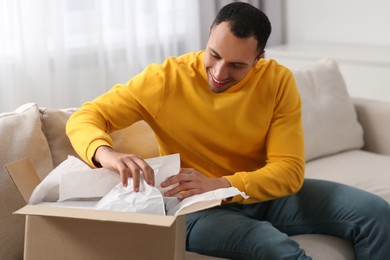 Photo of Happy young man opening parcel at home. Internet shopping