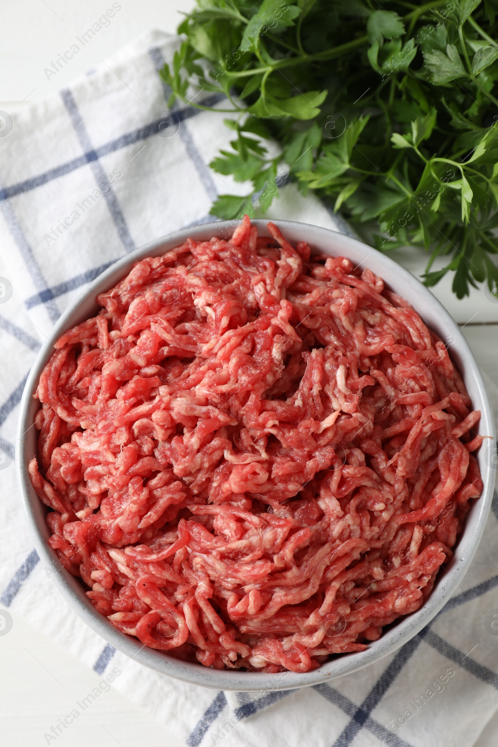 Photo of Raw ground meat in bowl and parsley on table, top view