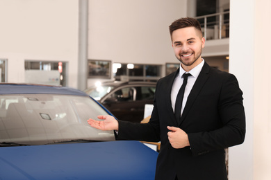 Young salesman near new car in dealership