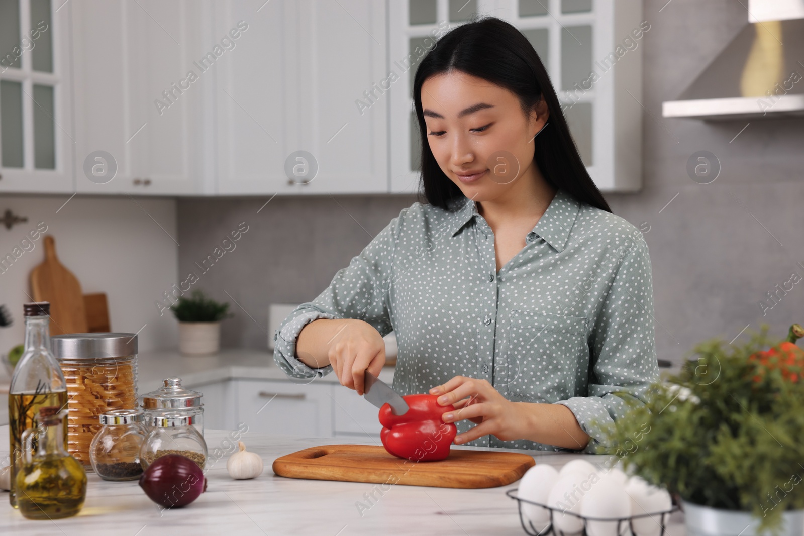 Photo of Cooking process. Beautiful woman cutting bell pepper at white countertop in kitchen