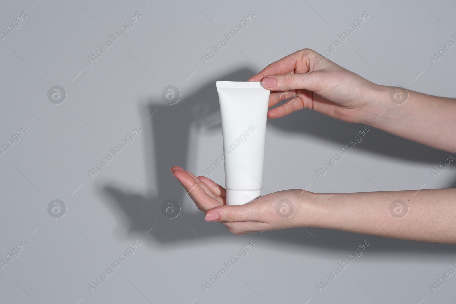 Photo of Woman holding tube of cream on grey background, closeup