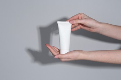 Photo of Woman holding tube of cream on grey background, closeup