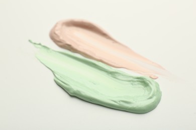 Photo of Strokes of pink and green color correcting concealers on white background