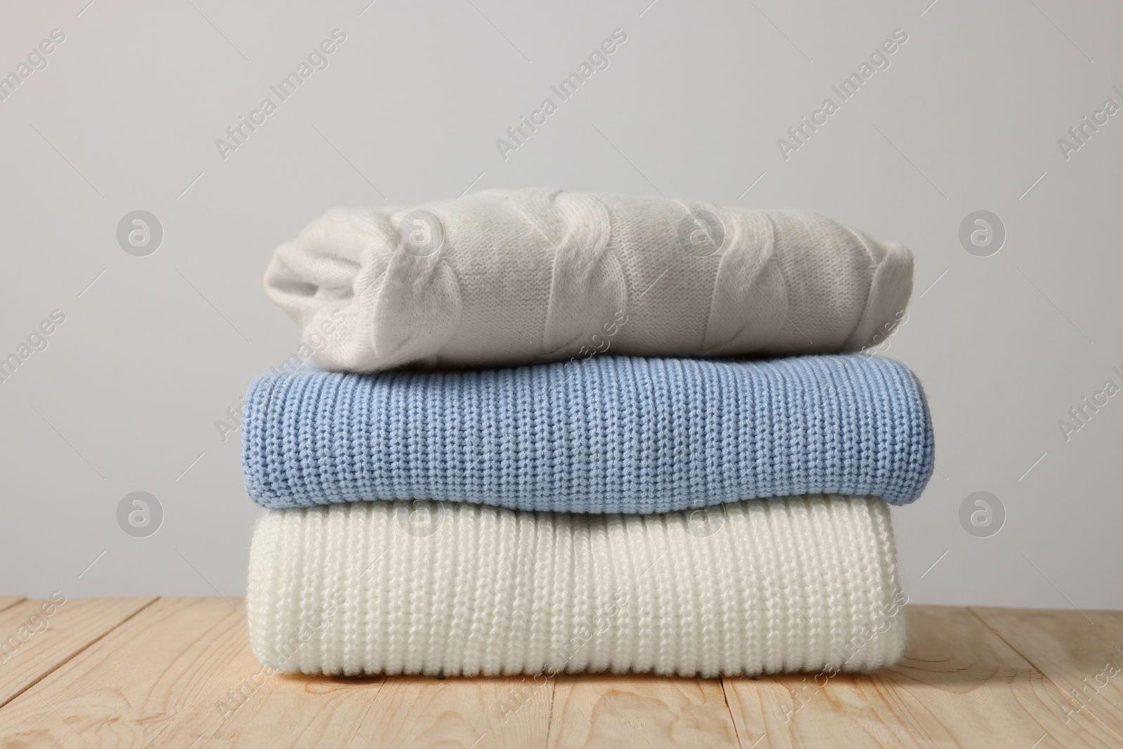 Photo of Stack of casual sweaters on wooden table against light background