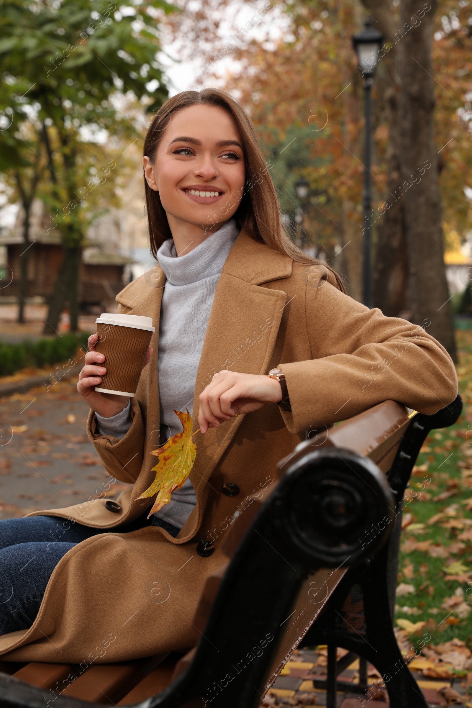 Photo of Beautiful young woman wearing stylish clothes with cup of coffee in autumn park