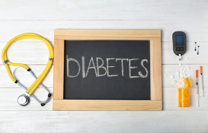 Photo of Flat lay composition with word "Diabetes", digital glucometer, stethoscope and medicine on wooden background