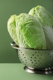 Fresh Chinese cabbages in colander on green background, closeup