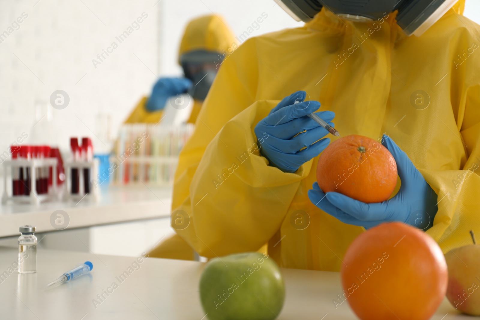 Photo of Scientist in chemical protective suit injecting orange at laboratory, closeup