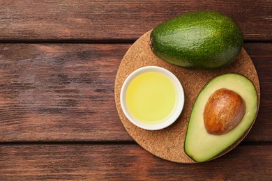 Photo of Cooking oil in bowl and fresh avocados on wooden table, top view. Space for text
