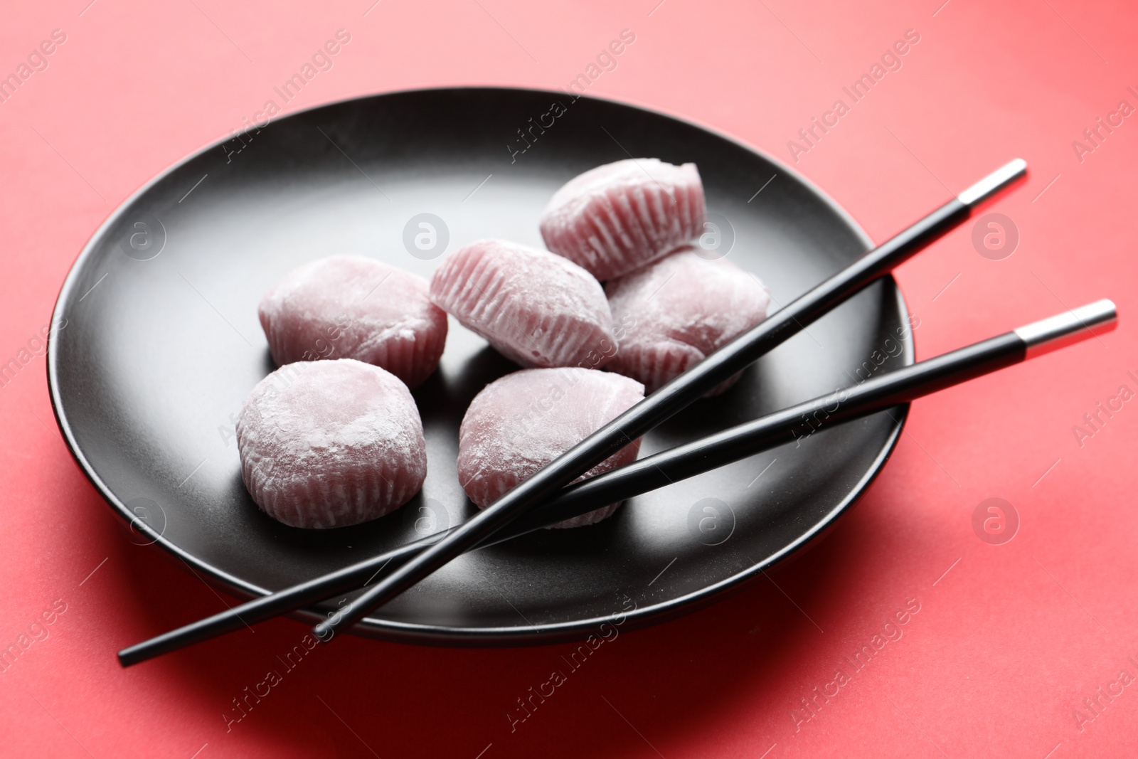 Photo of Black plate with delicious mochi and chopsticks on red background. Traditional Japanese dessert