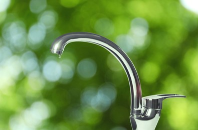 Image of Water drop flowing from tap outdoors on sunny day, bokeh effect