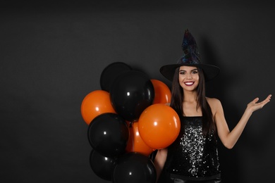 Photo of Beautiful woman wearing witch costume with balloons for Halloween party on black background