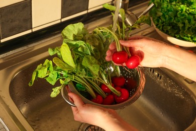 Photo of Woman washing fresh radishes in metal colander, closeup