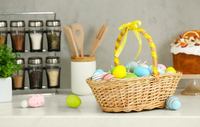 Easter basket with tasty painted eggs near cake on white countertop in kitchen