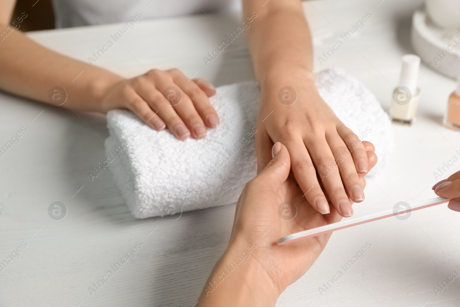 Photo of Manicurist filing client's nails at table, closeup. Spa treatment