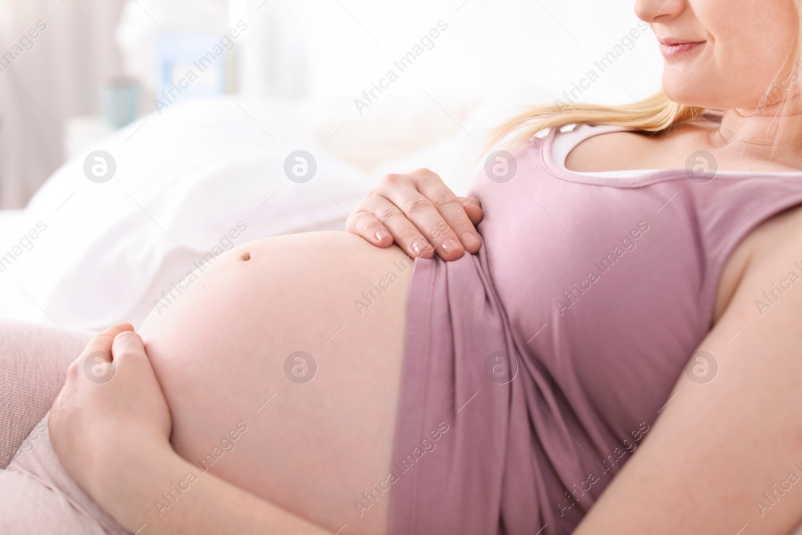 Photo of Pregnant woman resting on bed in light room, closeup