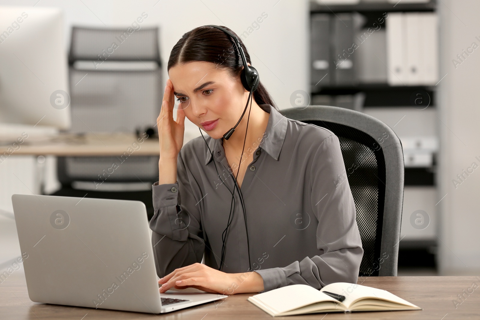 Photo of Stressed hotline operator with headset working on laptop in office