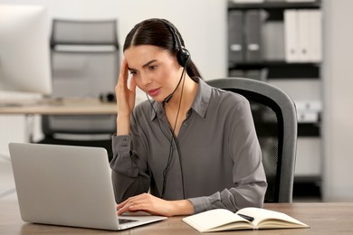 Photo of Stressed hotline operator with headset working on laptop in office