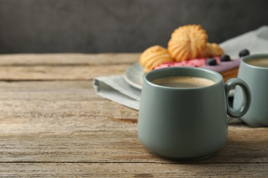 Photo of Aromatic coffee in cups, tasty eclairs and profiteroles on wooden table, space for text