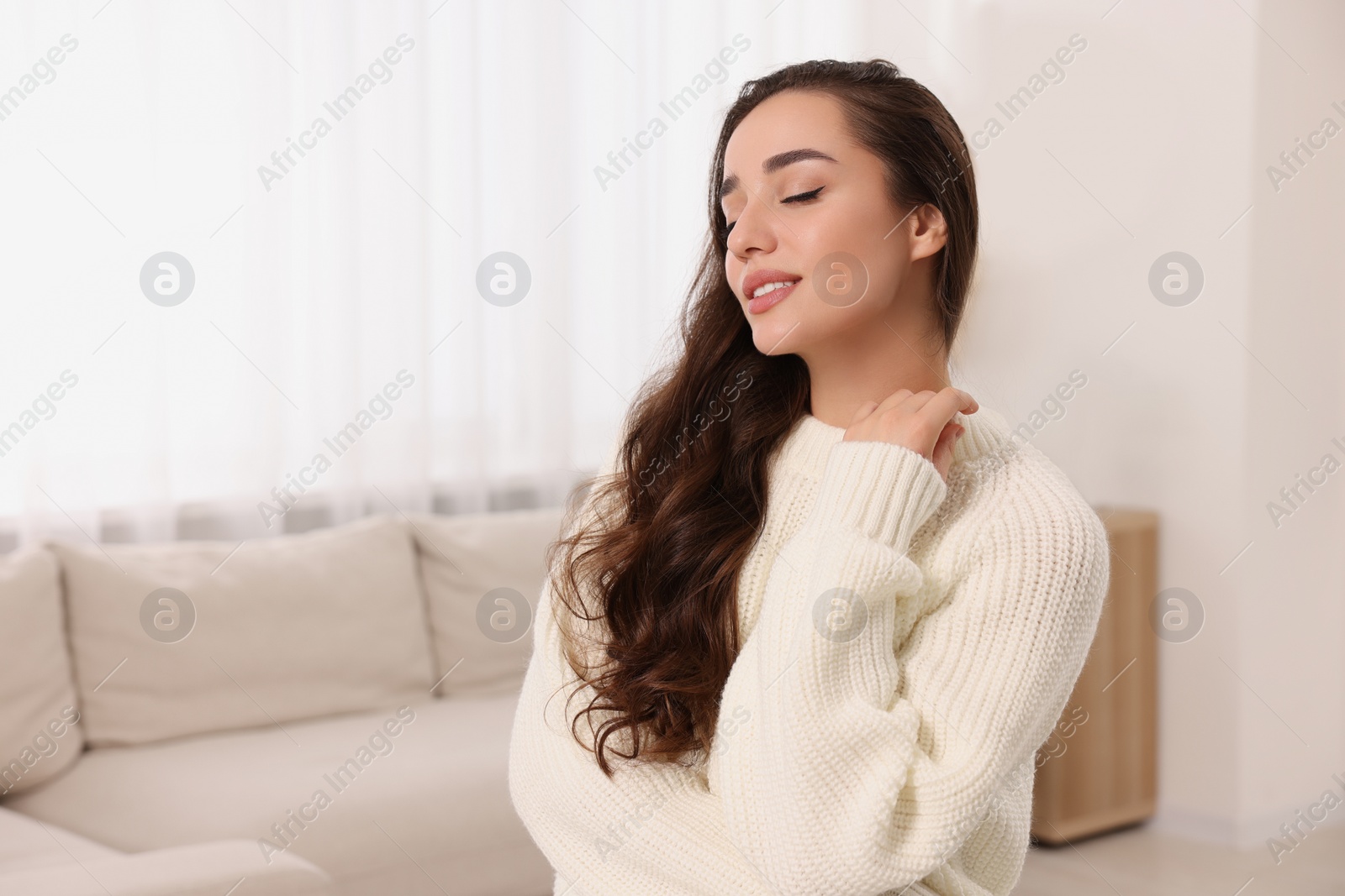 Photo of Beautiful young woman in stylish warm sweater at home, space for text