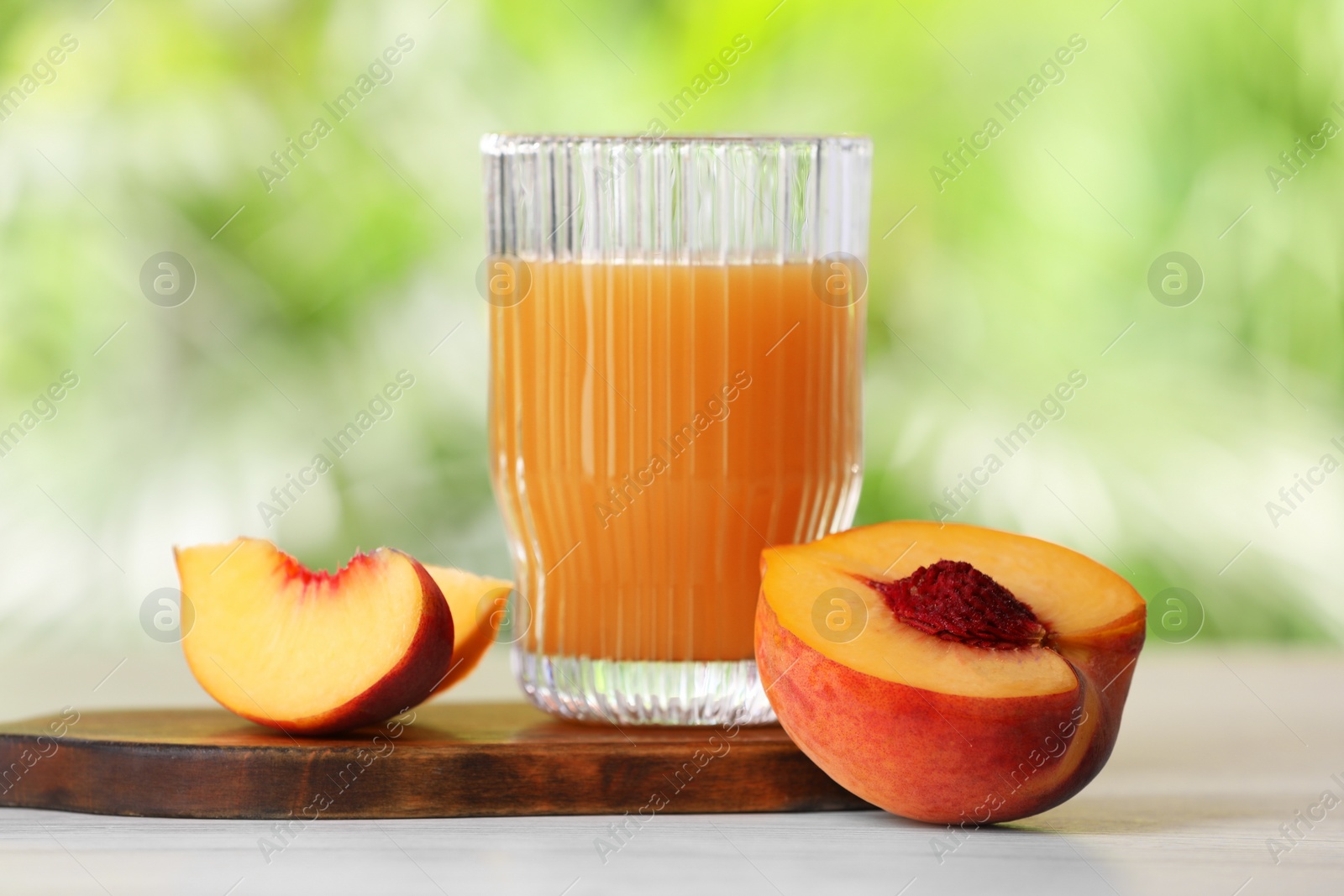 Photo of Glass of tasty peach juice and fresh fruit on white wooden table outdoors, closeup