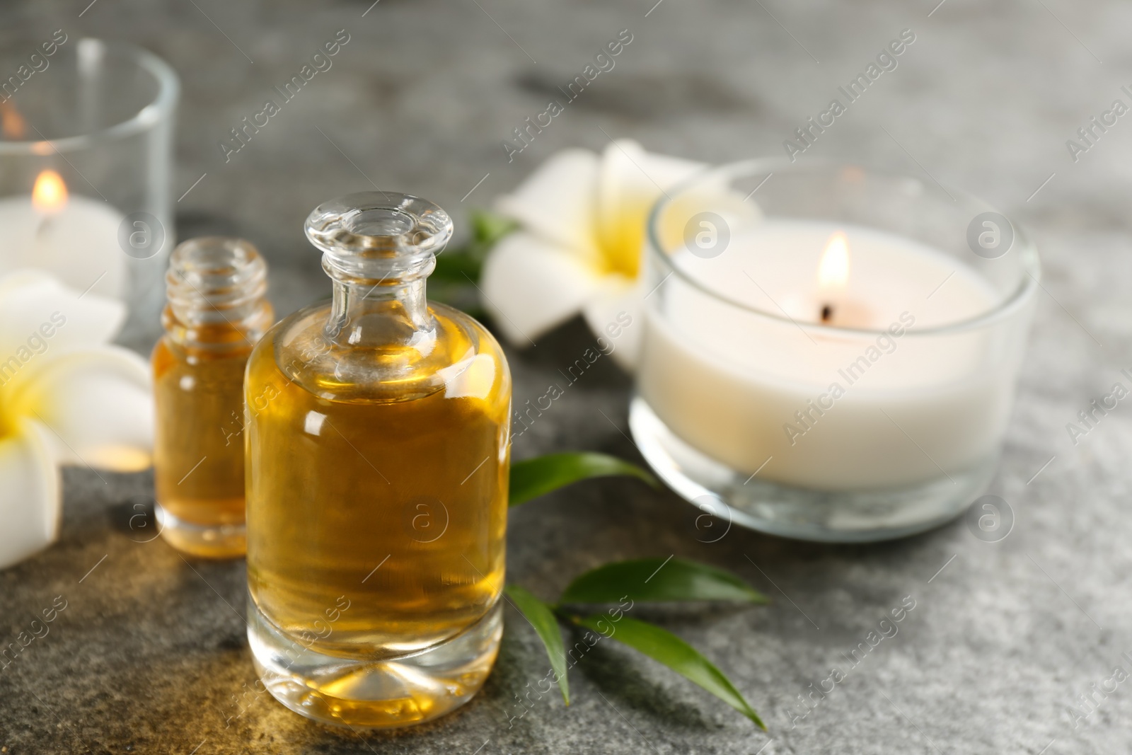 Photo of Beautiful spa composition with essential oil, candles and flowers on grey table, closeup