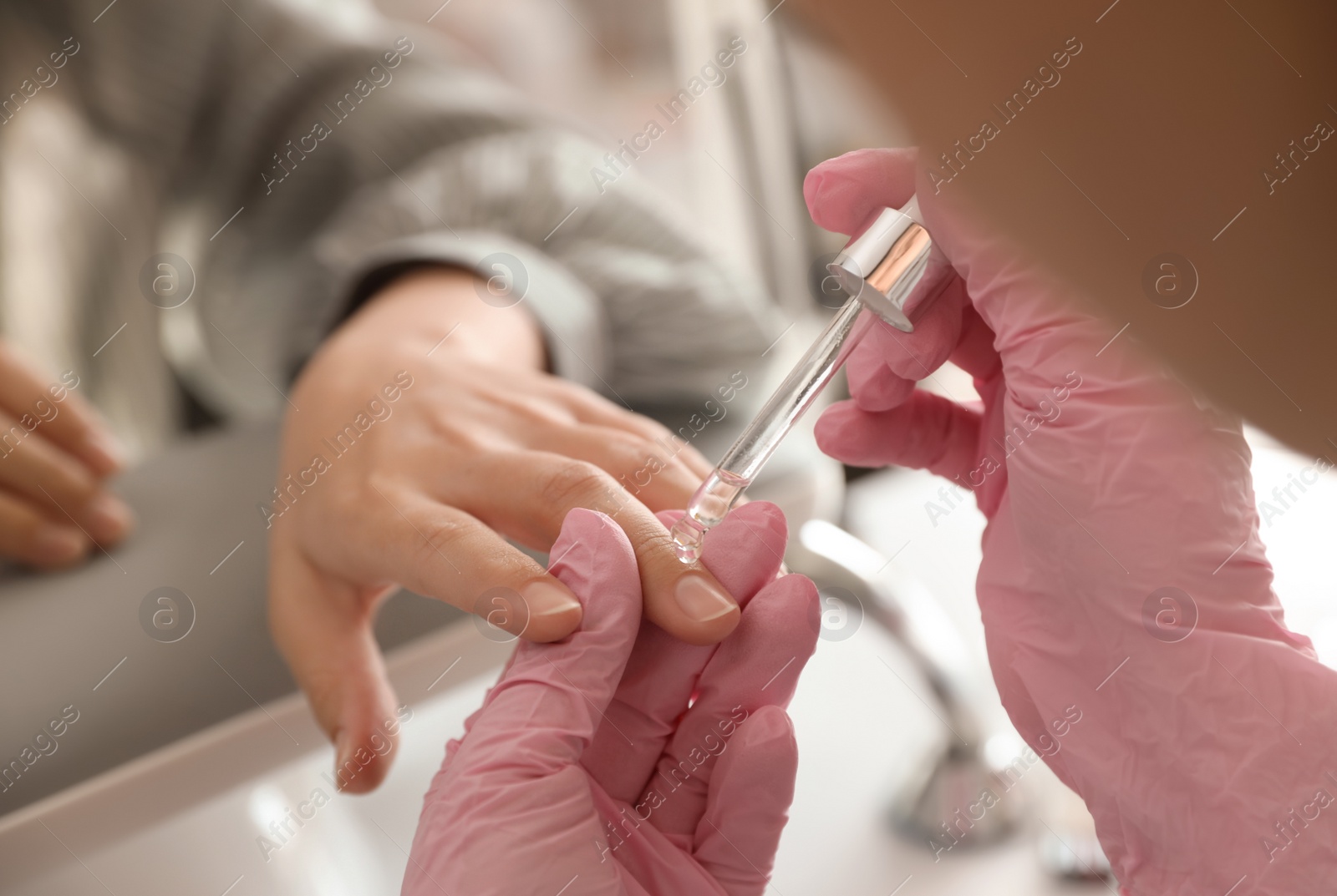 Photo of Professional manicurist pouring oil on client's nails in beauty salon, closeup