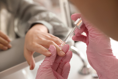 Professional manicurist pouring oil on client's nails in beauty salon, closeup