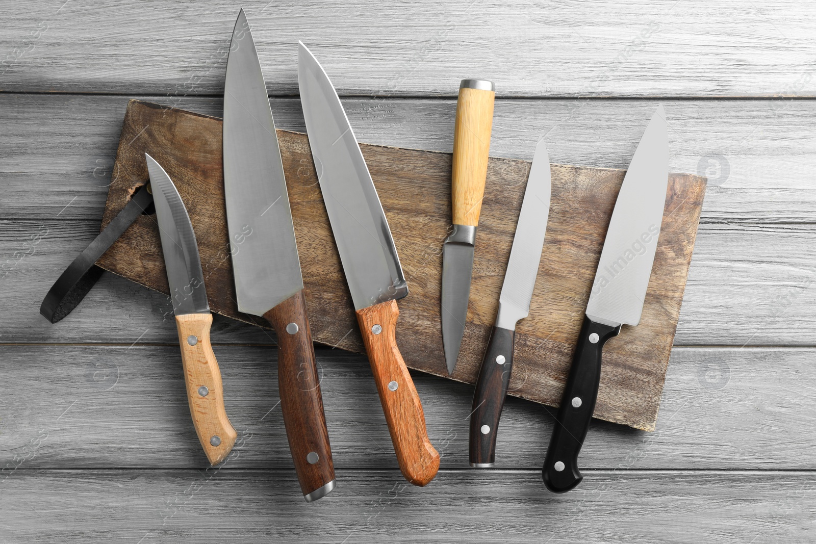 Photo of Many different knives and board on light wooden table, flat lay