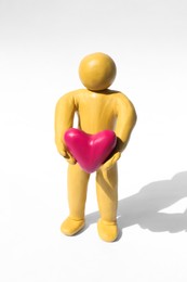 Yellow plasticine human figure with pink heart on white background