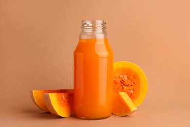 Tasty pumpkin juice in glass bottle and cut pumpkin on pale orange background
