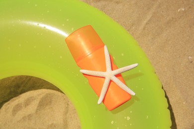 Photo of Sunscreen, starfish and inflatable ring on sand, top view. Sun protection care